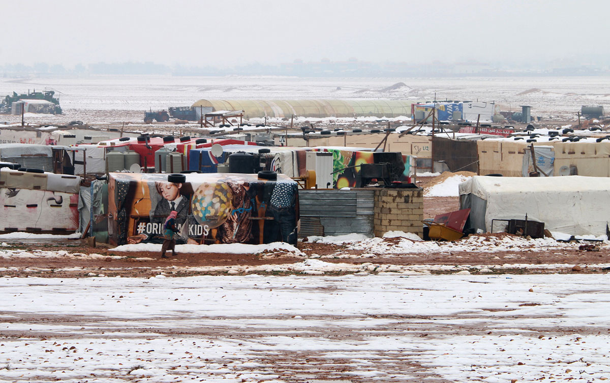 A Syrian refugee walks past makeshift shelters in an unofficial camp for refugees in Iaat in Lebanon's Bekaa valley, following a snow storm on January 8, 2019.