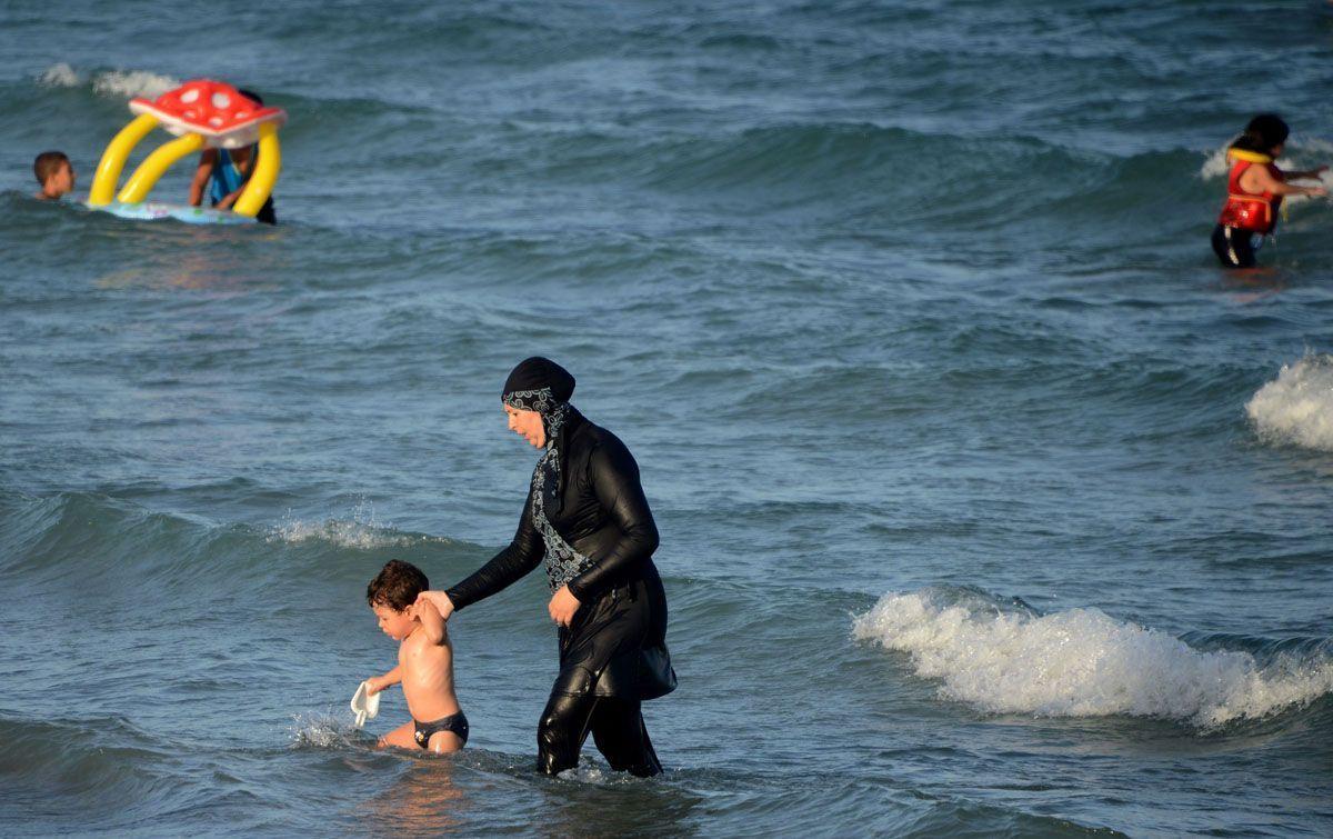 A Tunisian woman wearing a burkini, a full-body swimsuit designed for Muslim women, walks in the water with a child on August 16, 2016 at Ghar El Melh beach near Bizerte, north-east of the capital Tunis. / AFP / FETHI BELAID (Photo credit should read FETHI BELAID/AFP/Getty Images)