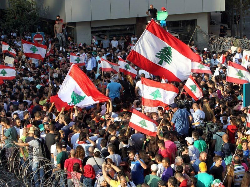 Lebanese protesters wave the national flag in front of a barbed wire fence during a demonstration, organized by You Stink campaign, to protest against the ongoing countrys trash crisis on August 23, 2015 in the capital Beirut. Protesters headed back to central Beirut in the morning, joining those who had spent the night there in tents afte