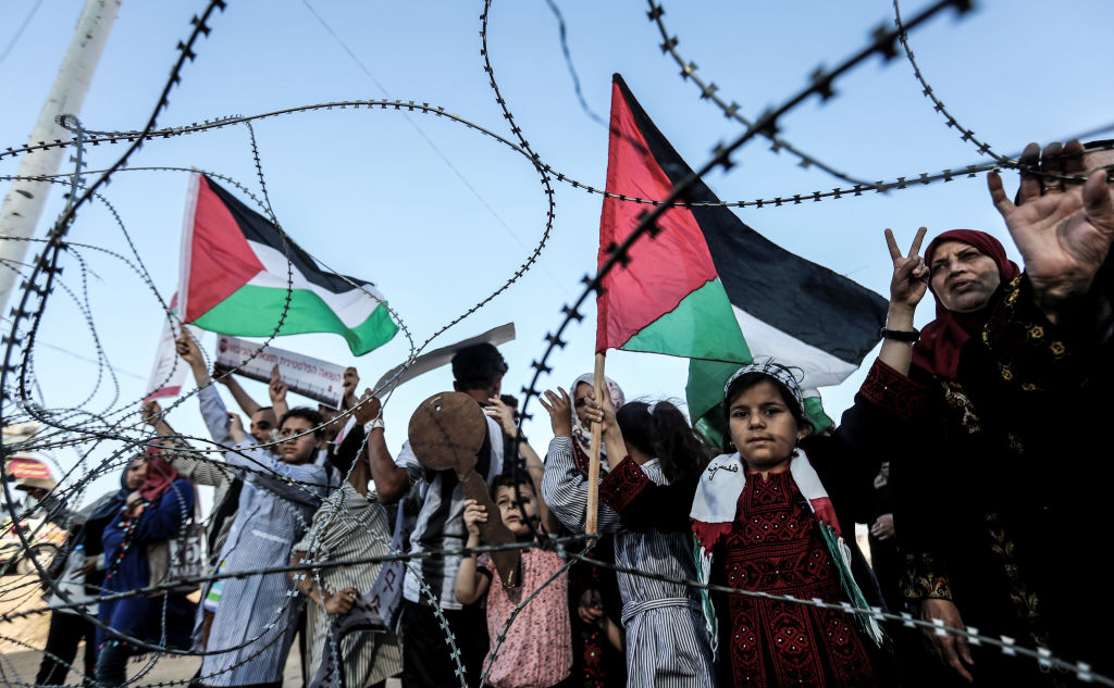 A girl raises a Palestinian flag as another Palestinian boy holds a wooden key symbolising the return as they stand with others before the barbed wire marking the border between the Gaza strip and Israel east of Gaza City on May 13 2018 during a demonstration anticipating the 70 years since the Palestinian Nakba or catastrophe of 1948 when