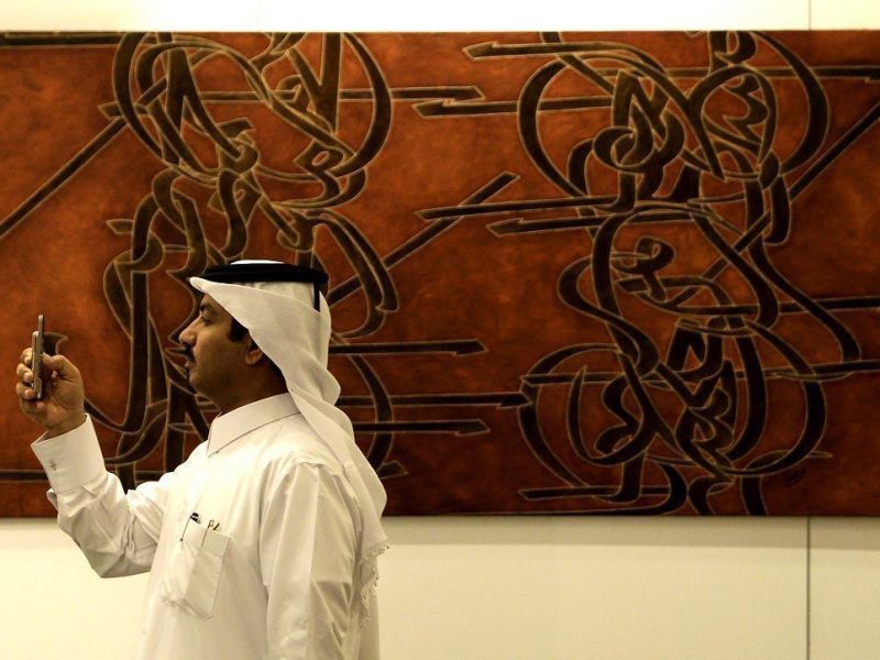 A visitor takes pictures with his mobile phone as he stands next to an artwork to be auctioned off by Sothebys at Arts of the Islamic World during a preview exhibition at a hotel in Doha