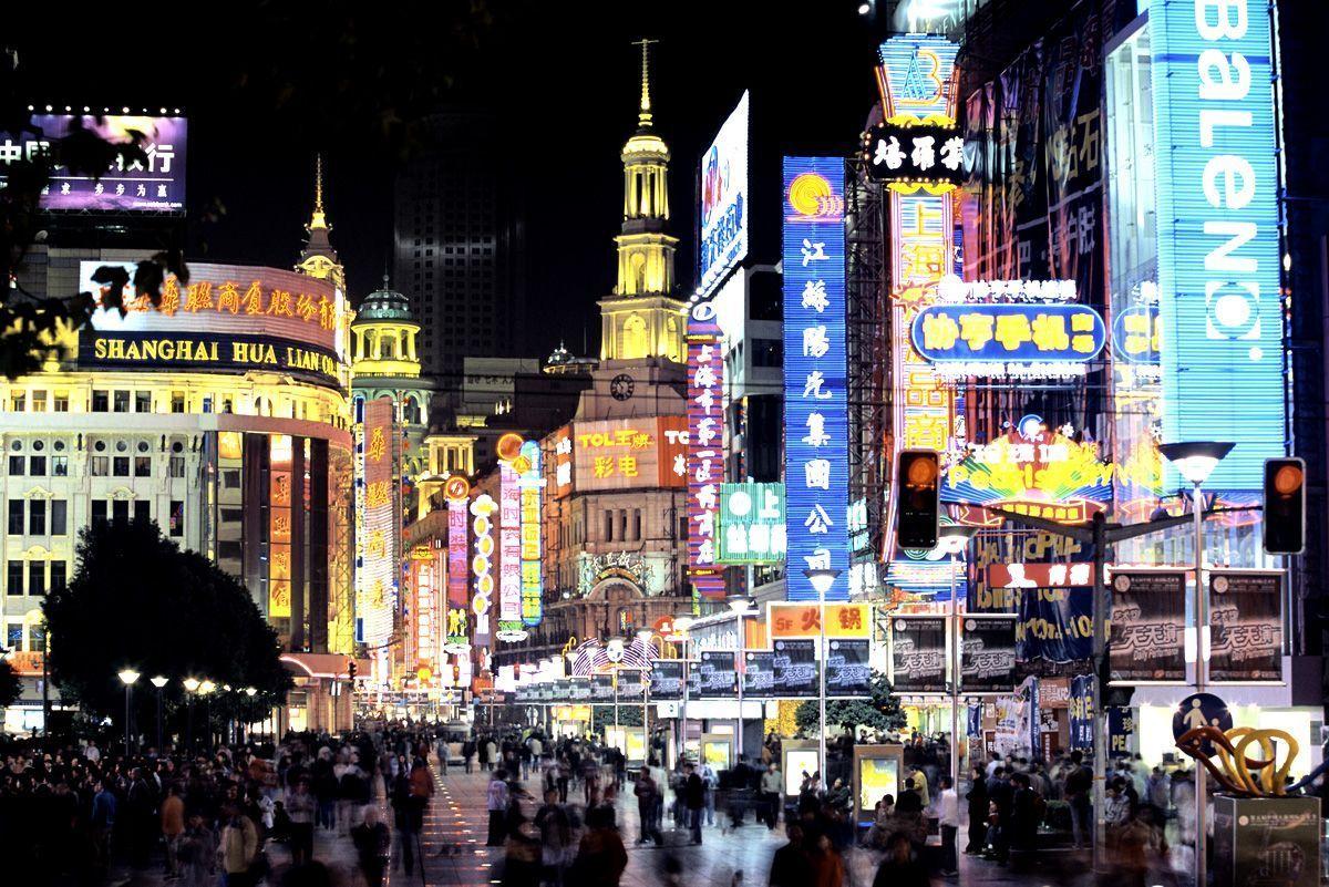 Bright neon lights stores and shoppers on Nanjing Road in Shanghai at night.