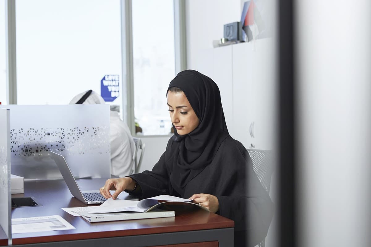 woman in hijab working on laptop in office with other people